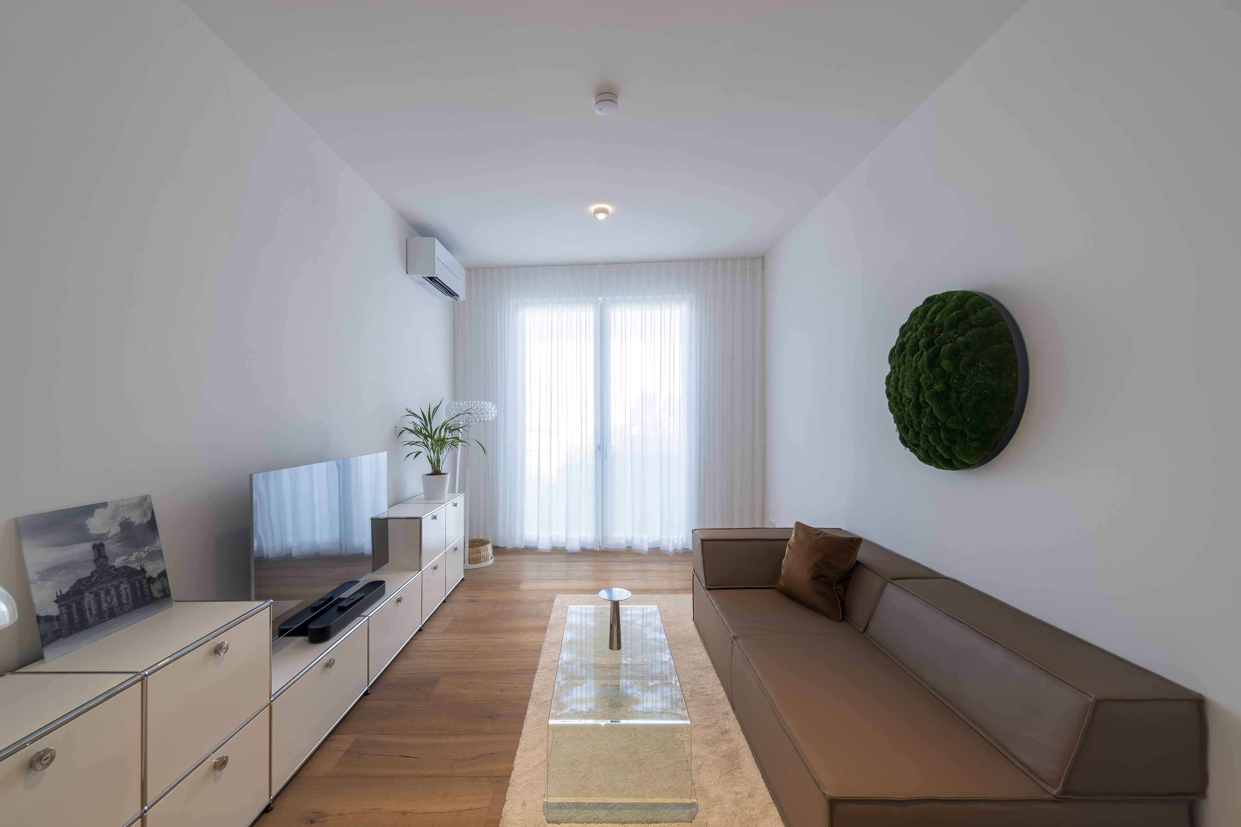 Haus L., Saarbrücken, Saarland — Wohnzimmer nach dem Einzug, mit Ledersofa, Sideboard und rundem Moosbild