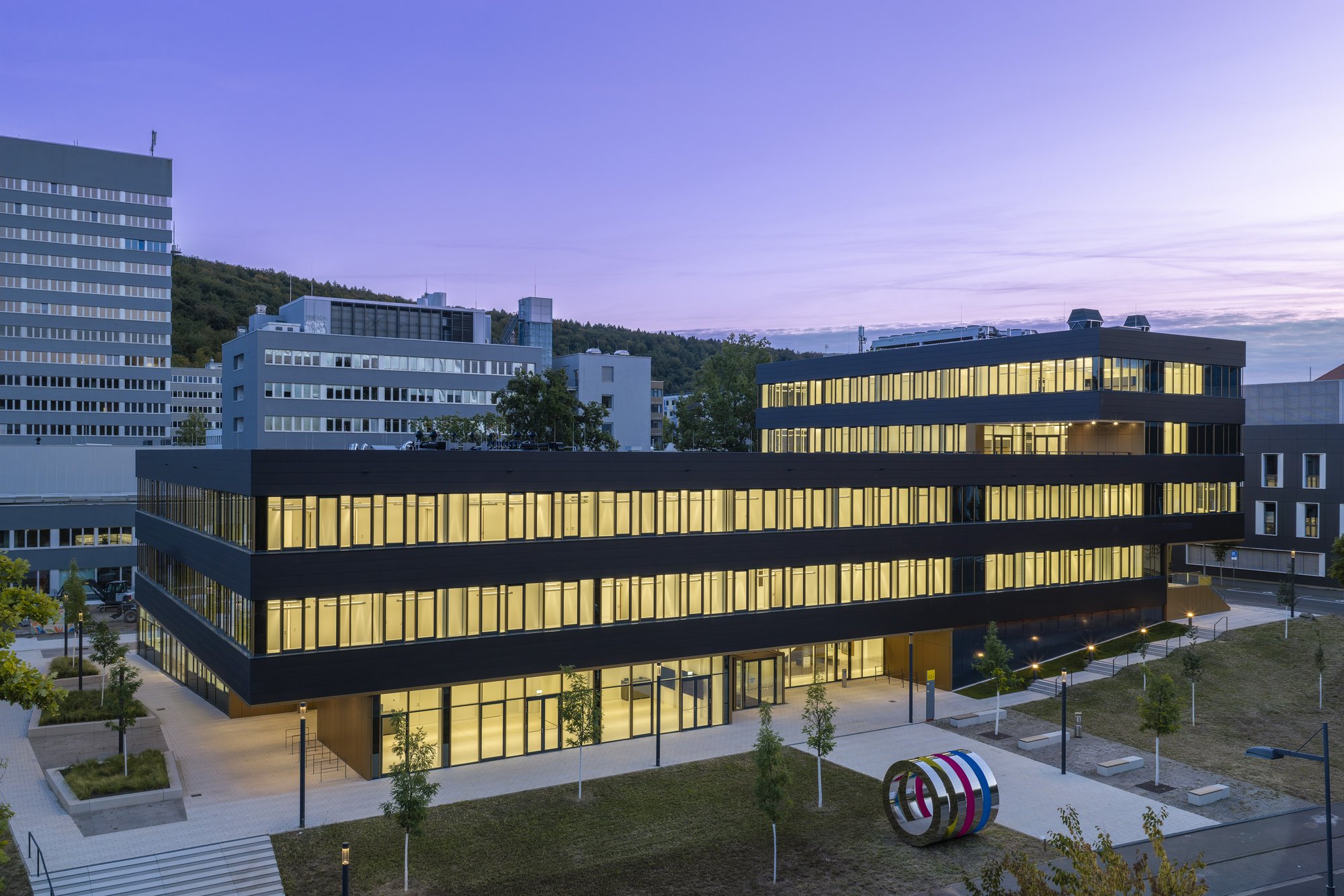 Architekturfotografie Zentrum für Biophysik ZBP, Saarbrücken — Erhöhte Abendansicht des beleuchteten Neubaus vor violettem Himmel