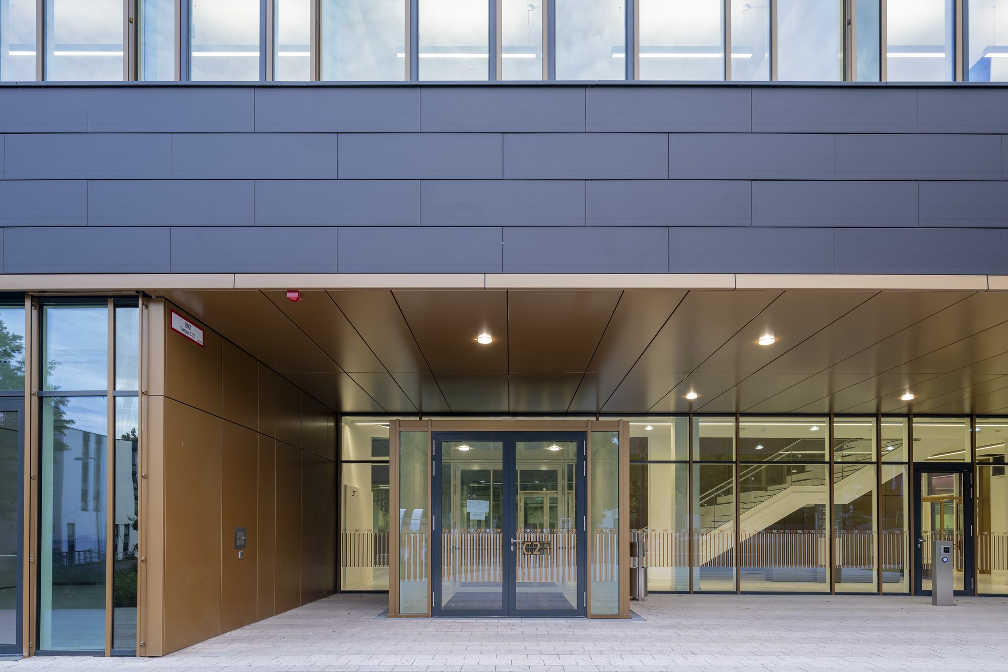 Architekturfotografie Zentrum für Biophysik ZBP, Saarbrücken — Haupteingang mit überdachter Vorzone, bronzefarbener Deckenbekleidung und Glastüren