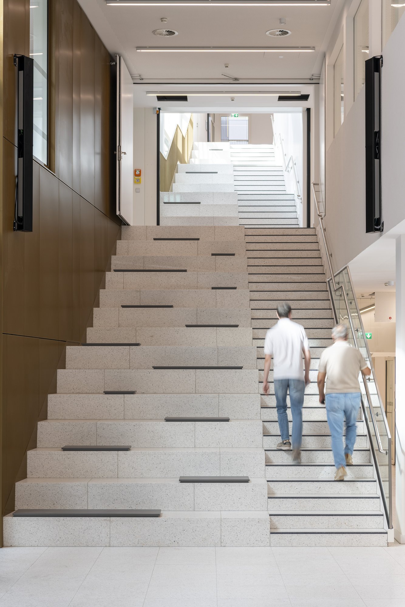 Architekturfotografie Zentrum für Biophysik ZBP, Saarbrücken — Treppe mit Sitzstufen, zwei Personen auf dem Weg ins Obergeschoss