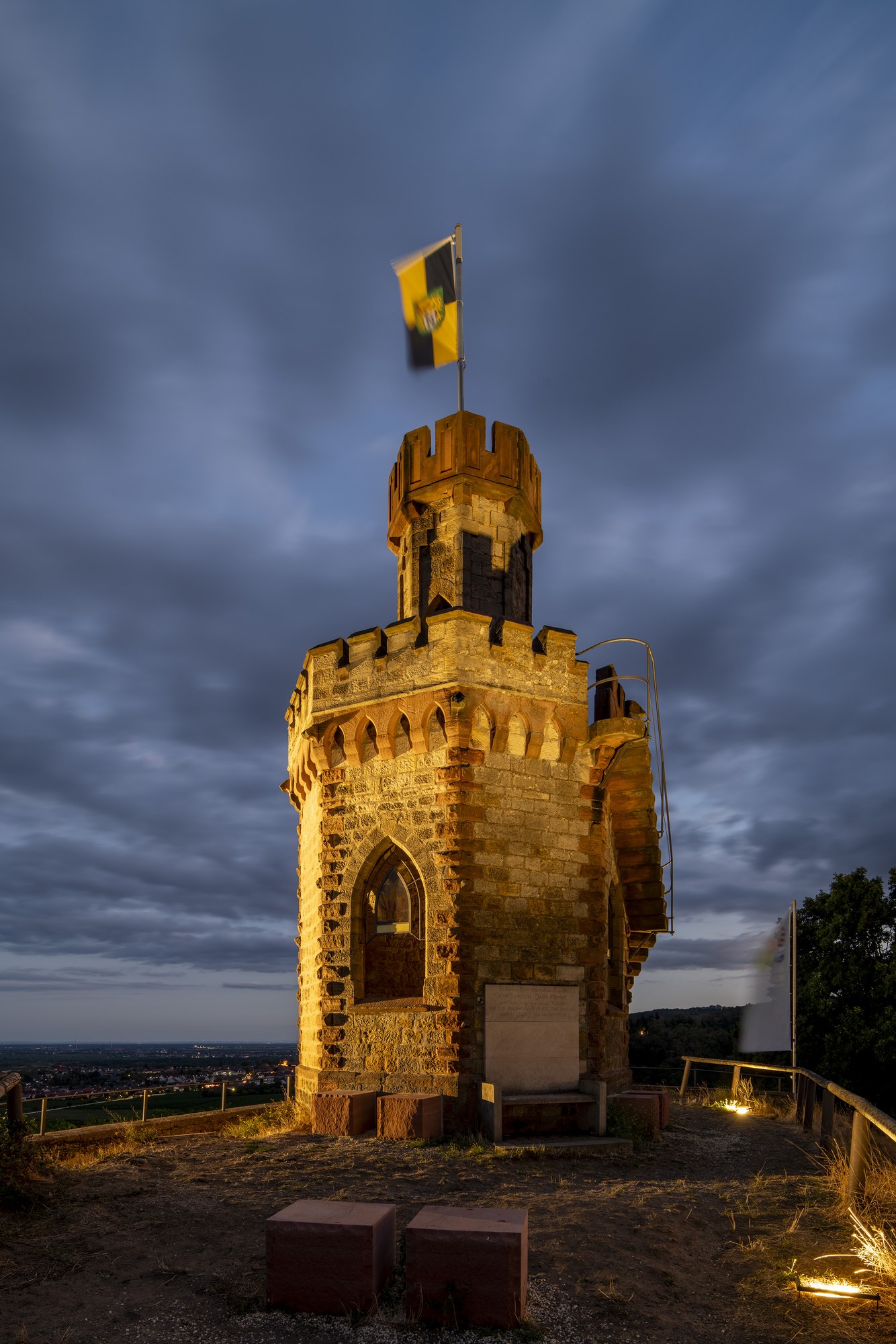Flaggenturm auf dem Fuchsmantel, Bad Dürkheim — der angestrahlte neugotische Turm mit gehisster Fahne vor dem Abendhimmel
