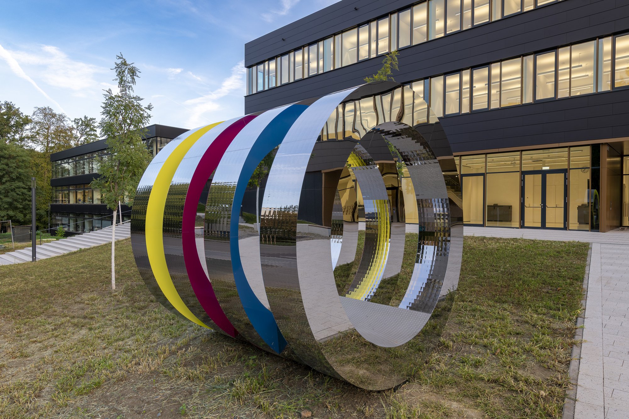 Architekturfotografie Zentrum für Biophysik ZBP, Saarbrücken — »PHI 42« von Winter/Hoerbelt, Ringe aus poliertem Edelstahl mit farbig gefassten Innenflächen, vor dem Gebäude