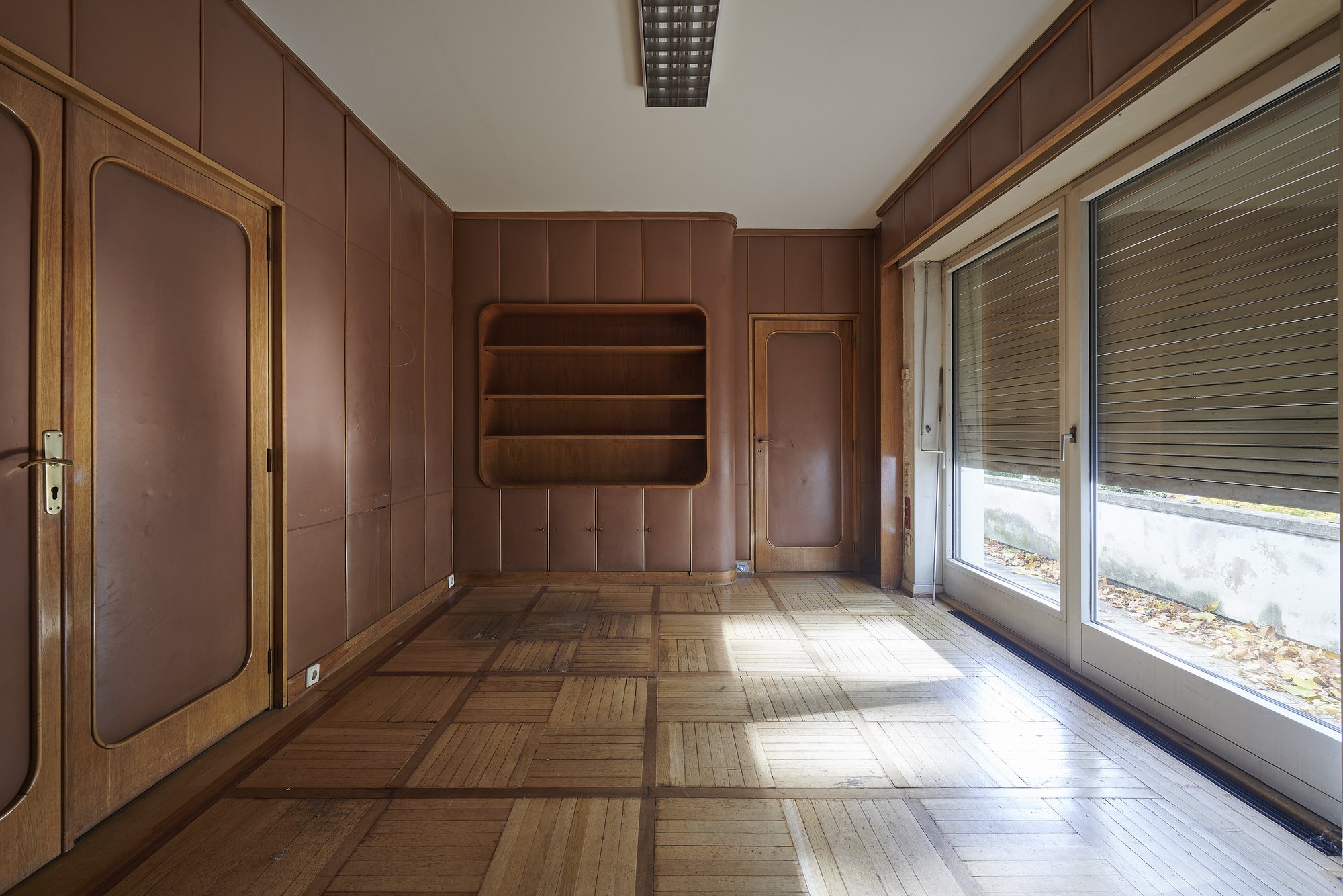 Ehemalige Französische Botschaft, Saarbrücken, Saarland — Zimmer mit brauner Wandbespannung, Einbauregal und Fensterfront