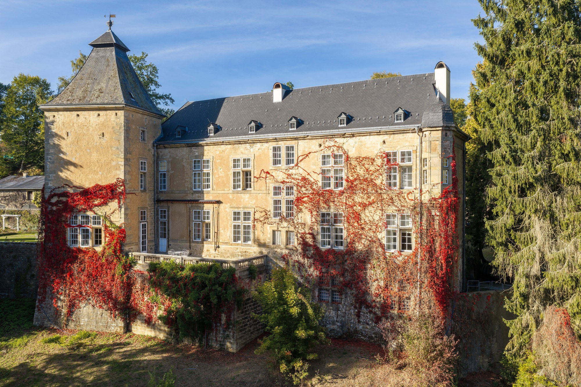 Architekturfotografie Renaissanceschloss Beaufort — Luftbild der Fassade mit Eckturm, überzogen von rotem Wildem Wein