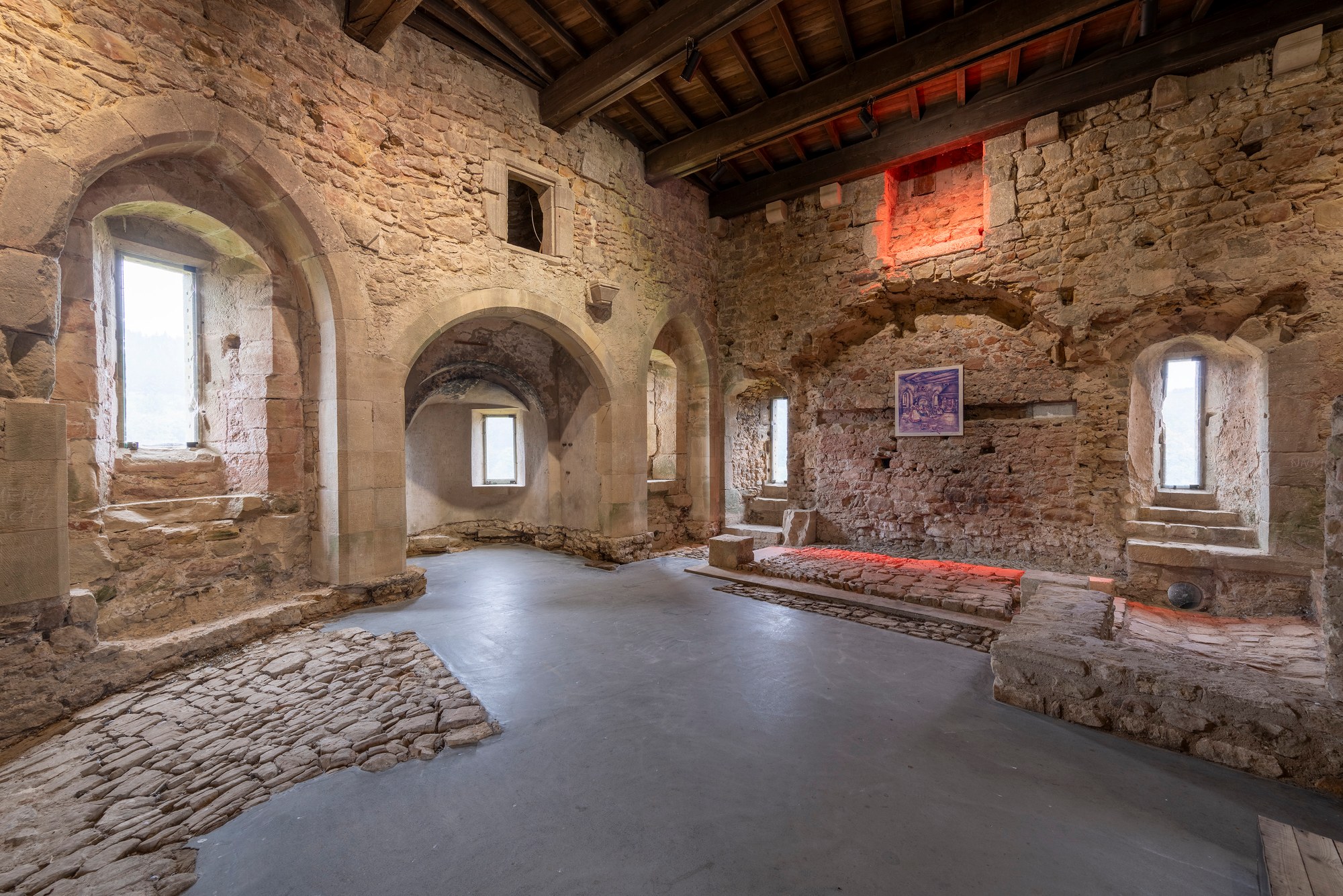 Architekturfotografie Criechinger Haus, Burg Larochette — die ehemalige Küche im Erdgeschoss mit Fensternischen, freigelegtem Pflaster und rot ausgeleuchteter Herdwand