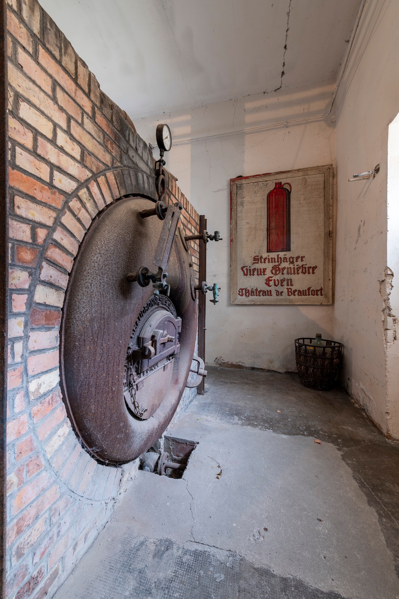 Architekturfotografie Renaissanceschloss Beaufort — Kessel mit runder Tür in gemauerter Ziegelwand, daneben ein altes Werbeschild für Steinhäger und Genever