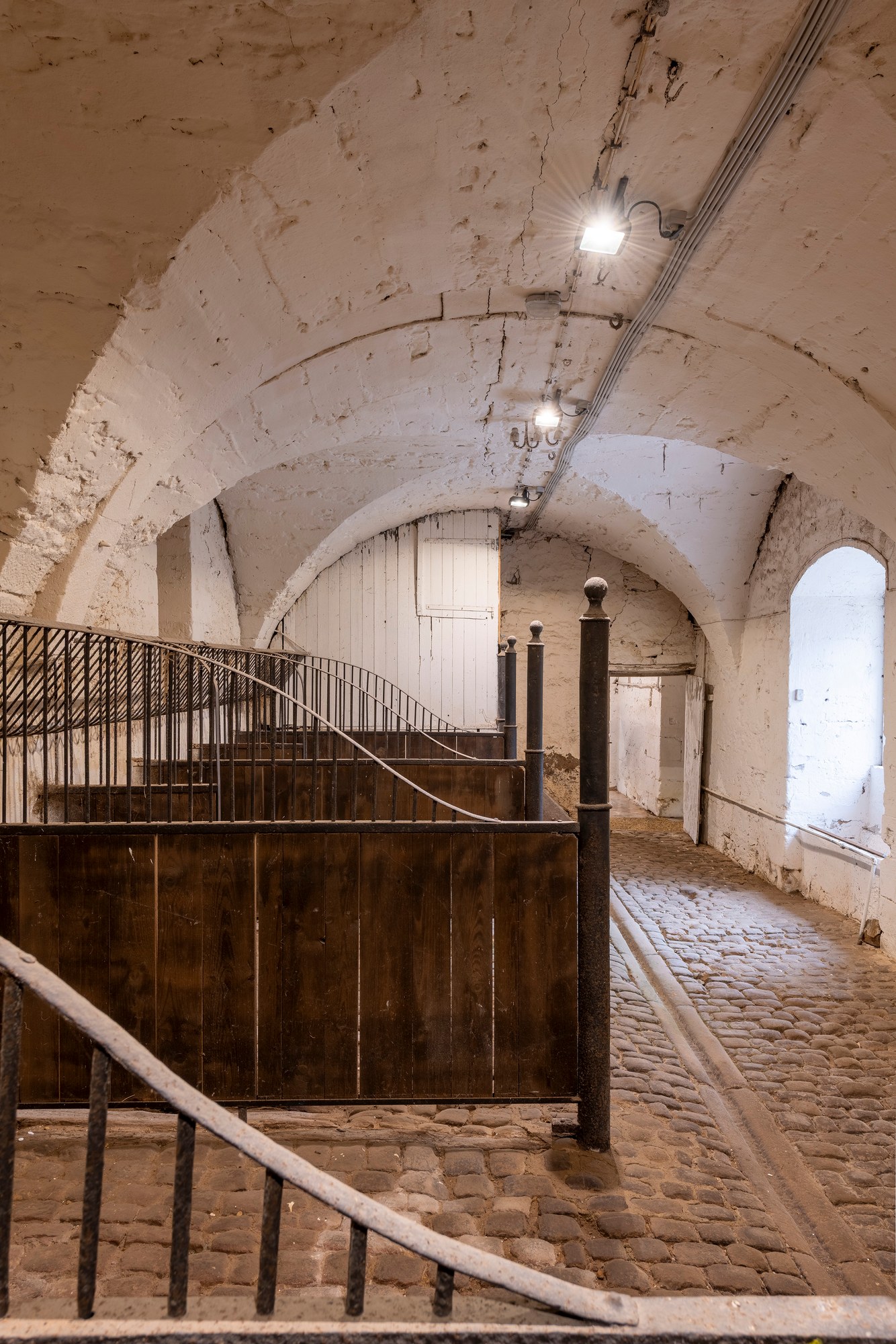 Architekturfotografie Renaissanceschloss Beaufort — gewölbter Pferdestall mit Holzboxen, Eisengittern und Kopfsteinpflaster